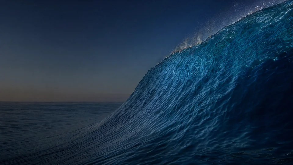 A monumental unbroken cobalt swell lifts at water level, carrying turquoise caustics beneath a silver ridge.