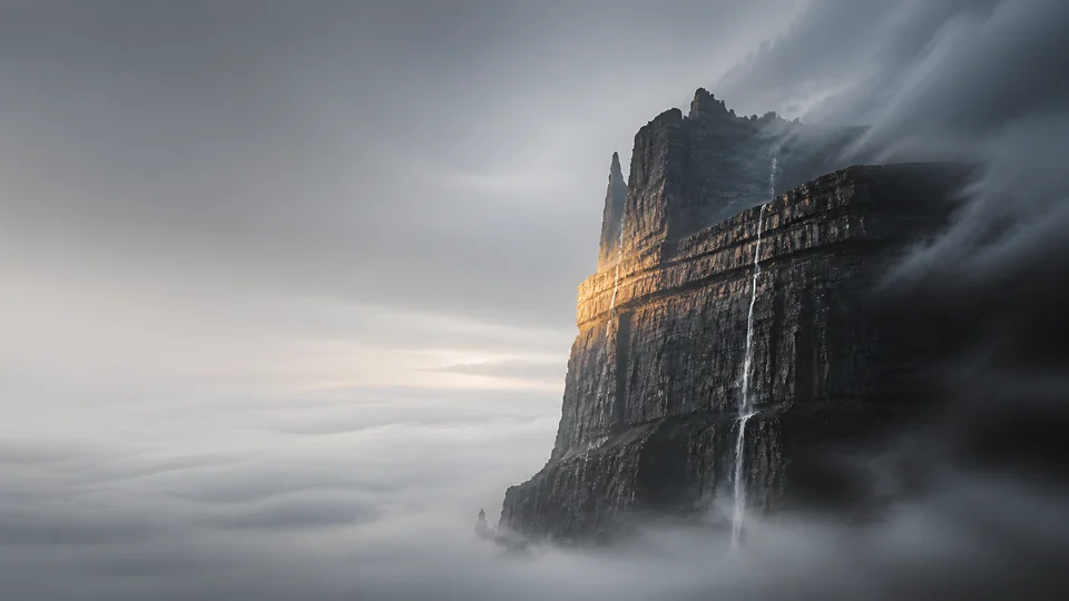 An invented basalt fin catches one amber seam above a pale sea of fog and vanishing waterfalls.