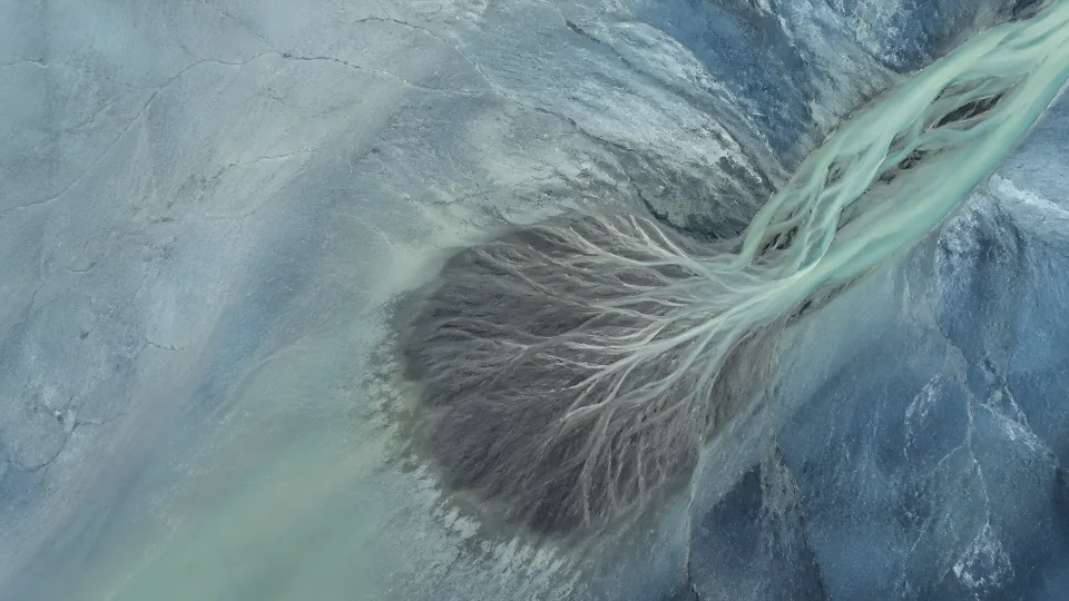 Jade meltwater releases a graphite silt fan across a blue-gray glacial field.